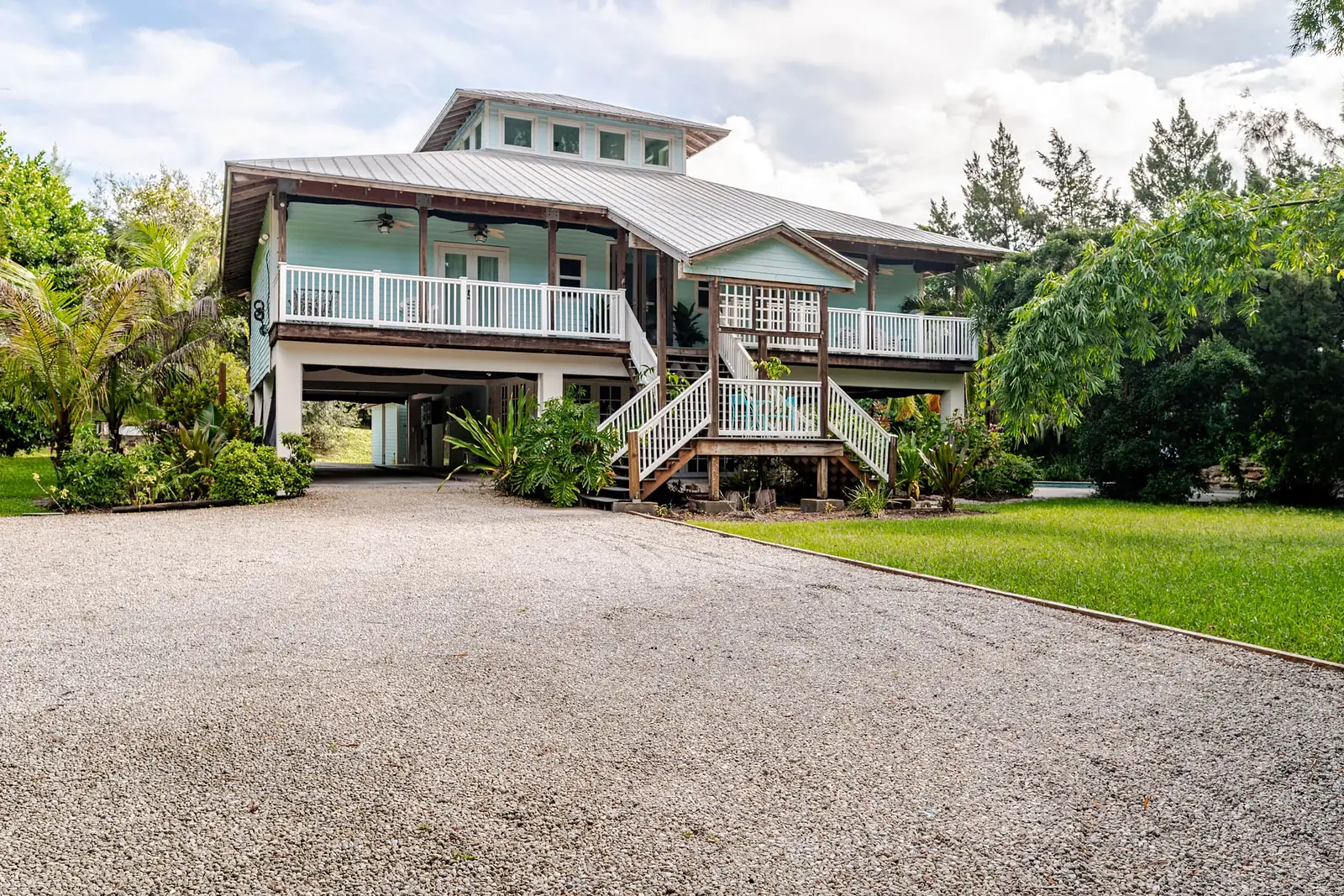 Raised house with wraparound porches, seen from the gravel drive