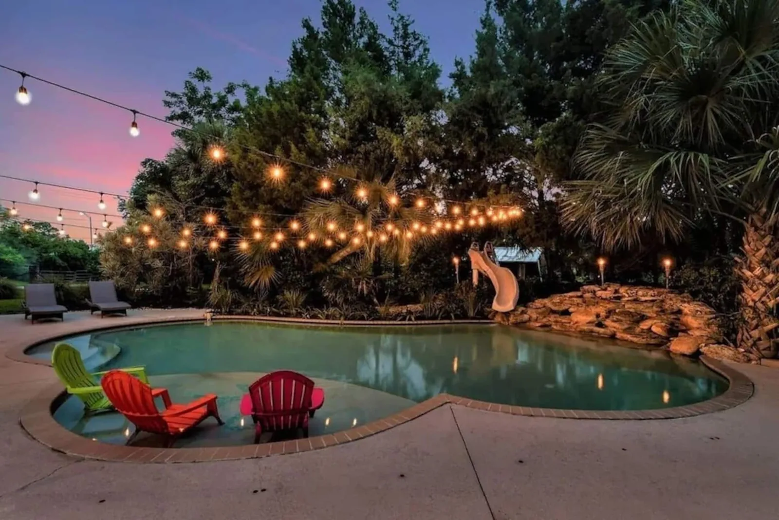 String-lit pool at sunset with bright chairs in the shallows