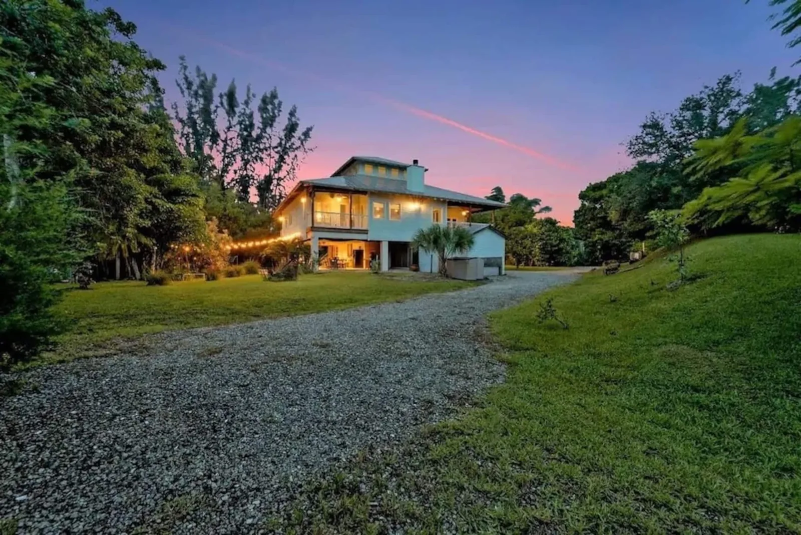 The house at dusk with its porch lights on, seen from the drive