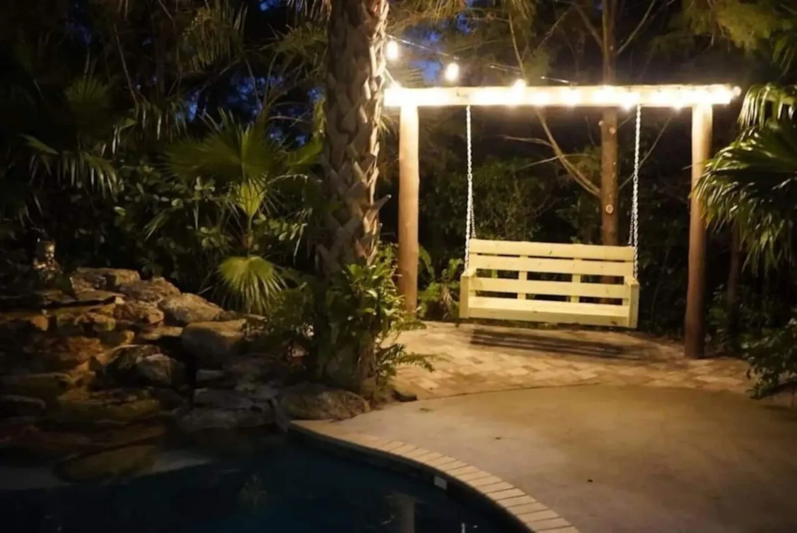 Lit swing frame beside the pool at night