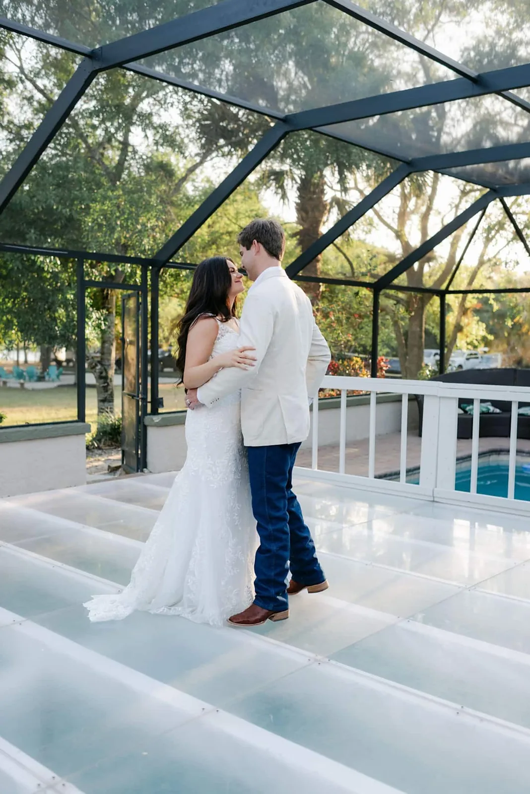 Bride and groom dancing on a clear floor laid over the screened pool
