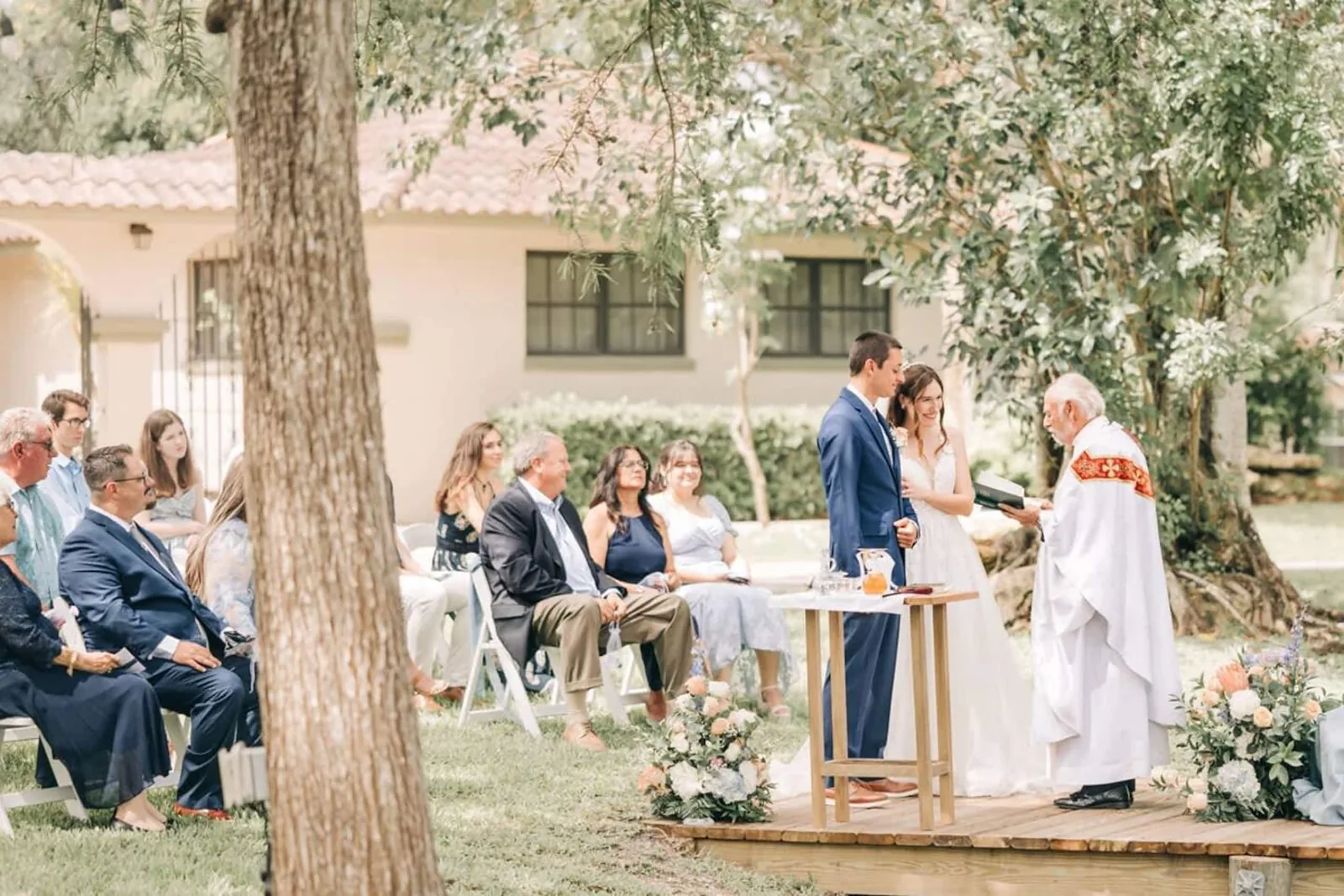 Ceremony with an officiant beneath the trees beside the house