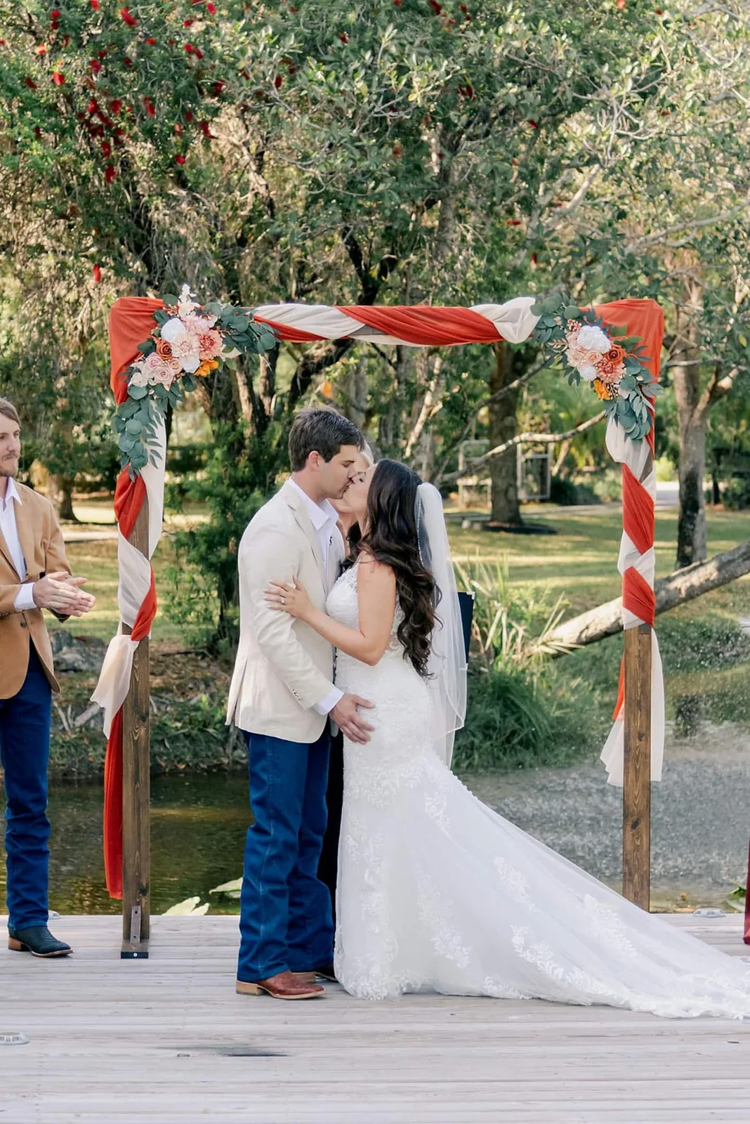 Bride and groom kissing under a draped floral arch on the pond dock